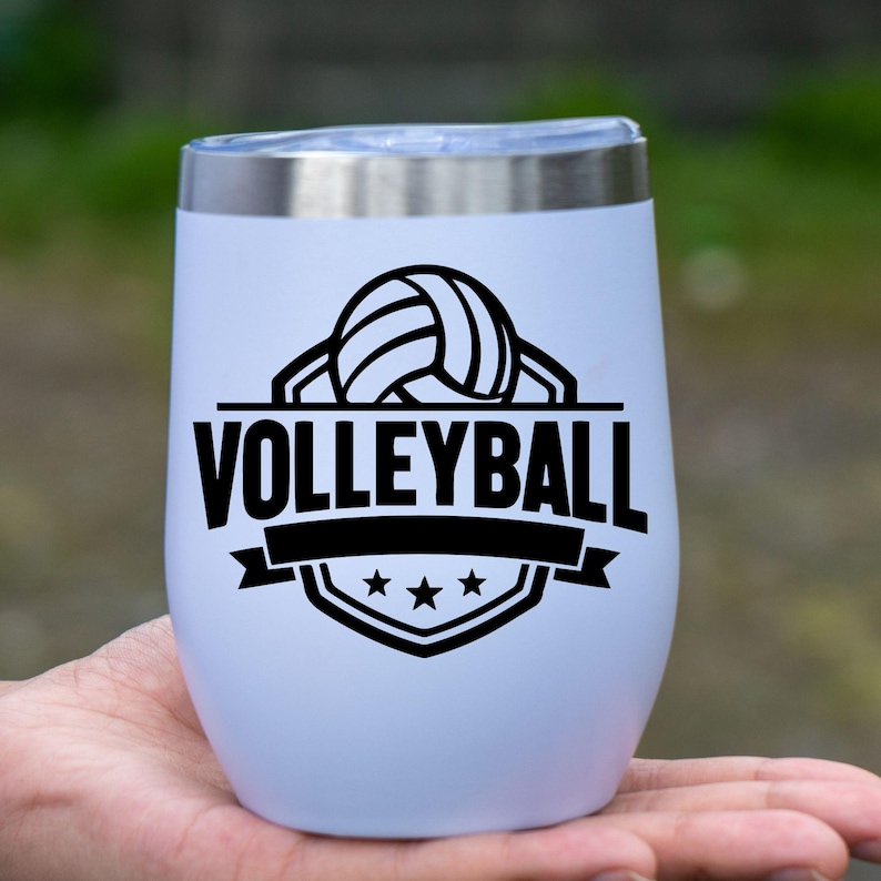 Op de afbeelding: Een witte ge&iuml;soleerde tumbler met een zilveren rand, met een zwarte volleybalafbeelding en het woord "VOLLEYBALL". Het ontwerp bevat een volleybal, banner en sterren.
