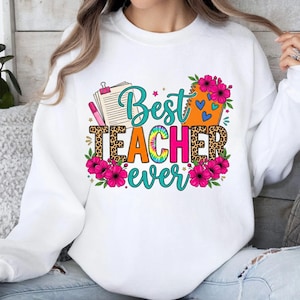 May include: White sweatshirt with a colorful graphic that reads "Best Teacher Ever." The design includes a leopard print, flowers, and a tie-dye effect. A notepad and pen are also featured in the design.