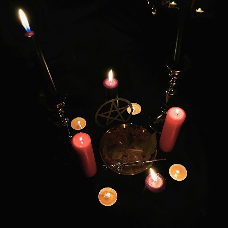 K&ouml;nnte beinhalten: Eine d&uuml;stere Szene mit brennenden Kerzen in verschiedenen Gr&ouml;&szlig;en und Farben, darunter Rot und Lila. Ein goldener Pentagramm und eine Schale befinden sich in der Mitte, vor einem schwarzen Hintergrund. Die Kerzen erzeugen eine mystische Atmosph&auml;re.