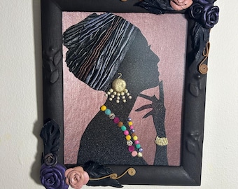 Könnte beinhalten: Schwarz gerahmtes Kunstwerk mit einer Silhouette einer Frau mit Kopftuch, Ohrringen und Halskette. Der Rahmen ist mit geformten Blumen in Lila- und Rosatönen verziert. Der Hintergrund ist ein zartes Rosa.