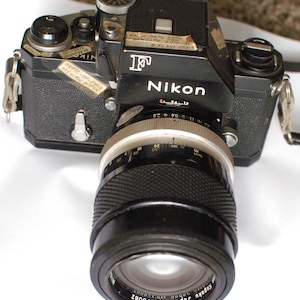 Black Nikon F Camera No. 6841486 with FTN Finder and Nikon 135mm f2.8 Nikkor Lens No. 178082 and off brand strap.