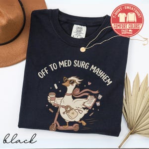 May include: A black t-shirt featuring a graphic of a goose wearing sunglasses and a scarf, riding a scooter while holding a coffee cup and a patient chart. The text reads OFF TO MED SURG MAYHEM. The shirt has a Comfort Colors brand label at the neck.
