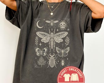 May include: Dark gray Comfort Colors t-shirt with a detailed white insect and botanical illustration. The design includes a moth, butterflies, beetles, and a crescent moon. The shirt has a vintage, worn look and features the text "pepper" and a Comfort Colors logo.