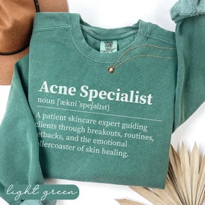 Sage green "Acne Specialist" sweatshirt with definition and light green text.