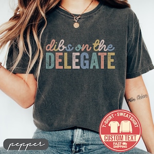 May include: A white ceramic mug with a black handle and the text "But First, Coffee" in a bold, black font. The mug is set against a blurred background, suggesting a cozy setting. The mug appears to be approximately 4 inches tall.