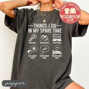 May include: Dark gray Comfort Colors t-shirt with the text "---THINGS I DO--- IN MY SPARE TIME" and illustrations of bugs. The shirt also has the words "FIND BUGS", "WATCH BUGS", "STUDY BUGS", "TALK ABOUT BUGS", "THINK ABOUT BUGS", and "DREAM ABOUT BUGS".