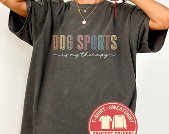 May include: Pepper-colored t-shirt with the text "DOG SPORTS is my therapy" in a rainbow font. A red Comfort Colors logo is in the lower right corner. The shirt is a Comfort Colors brand.