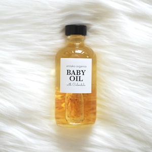 Pu&ograve; includere: Una bottiglia di vetro trasparente di olio per bambini con un tappo nero. L'etichetta riporta "anitako organics BABY OIL with Calendula".