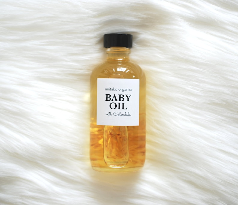 Pu&ograve; includere: Una bottiglia di vetro trasparente di olio per bambini con un tappo nero. L'etichetta riporta "anitako organics BABY OIL with Calendula".