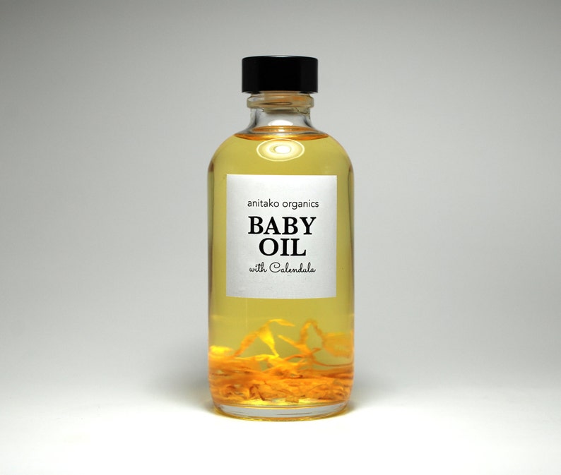 Pu&ograve; includere: Una bottiglia di vetro trasparente di olio per bambini con un tappo nero. L'etichetta recita "anitako organics BABY OIL with Calendula".