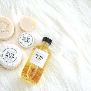 Pu&ograve; includere: Due saponette per bambini rotonde e bianche con la scritta "antako organics BABY SOAP with Calendula" e un orso dei cartoni animati su una saponetta. Una bottiglia di vetro trasparente di olio per bambini con la scritta "antako organics BABY OIL with Calendula" e un fiore giallo all'interno.