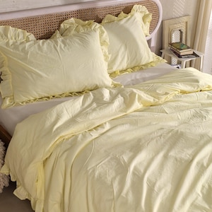 May include: A bed is made with a pale yellow duvet cover and matching pillowcases. The pillowcases and the edge of the duvet cover have a ruffled trim. The headboard is made of woven wicker.