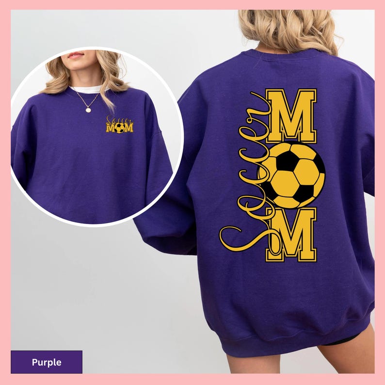 May include: A purple sweatshirt with "Soccer Mom" printed on the back in yellow and black. The design includes a soccer ball and the words "Soccer Mom". The front of the sweatshirt has the words "Soccer Mom" in a smaller design.