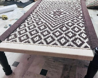 May include: A woven bed frame with a geometric pattern in brown and white. The frame has dark wooden legs and a woven surface, showcasing a traditional design. The bed frame is a unique piece of furniture.