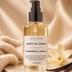 May include: A clear glass bottle of body oil serum with a black pump top. The label reads "jena's corner BODY OIL SERUM CASHMERE & VANILLA" and lists ingredients. The bottle contains 4 ounces of product.