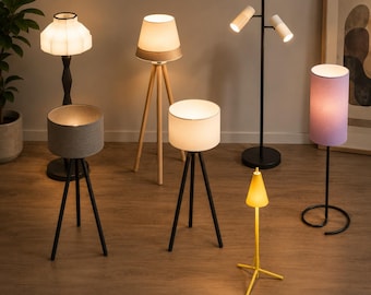 May include: A collection of seven floor and table lamps featuring various designs, including tripod bases in wood and black metal, a dual-head black floor lamp, a tall lamp with a pleated shade, and a small yellow lamp with a conical shade.