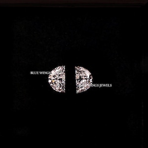 May include: A black jewellery box displaying a pair of diamond earrings. The earrings are arranged in a semi-circular design. The text "BLUE WINGS" and "INGS JEWELS" are visible on the box.