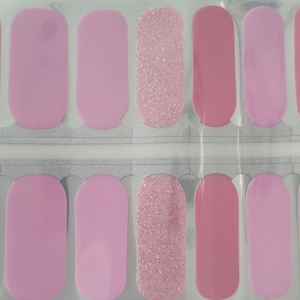 May include: A sheet of pink nail polish strips in various shades. The strips include solid light pink, medium pink, and glittery pink designs. The nail polish strips are arranged in a grid pattern, ready for application.