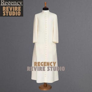 May include: Cream-colored, long-sleeved robe with a mandarin collar and button-down front. The robe is displayed on a mannequin with a wooden stand. The text "Regency Revire Studio" is visible in the upper left and lower center.