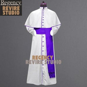 May include: A white clerical robe with a purple sash and trim. The robe has a high collar and is buttoned down the front. The image includes the text "Regency Revire Studio".