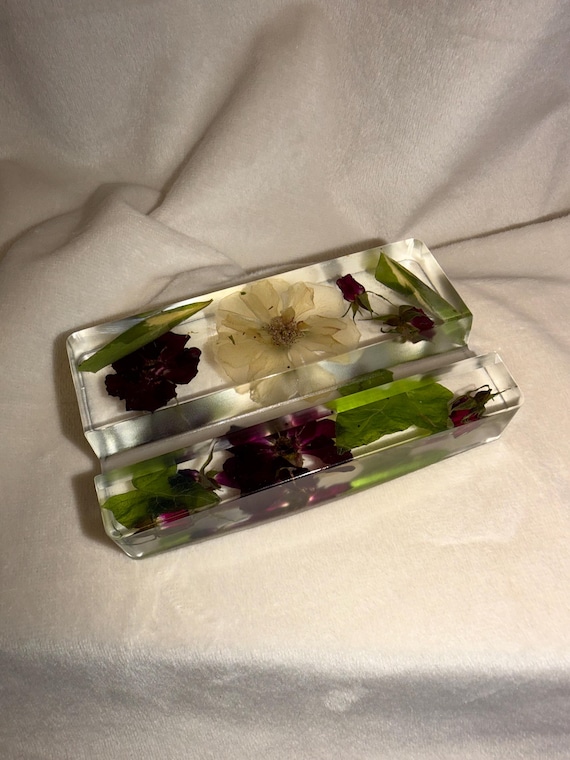 Real pressed botanicals suspended in clear resin make this phone stand a tiny terrarium-like nature display you actually use every day.