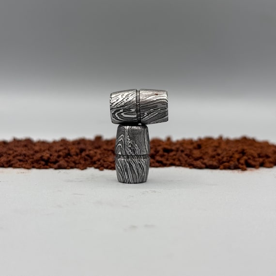 Hand-forged Damascus steel lanyard bead — a tiny but intricate piece of wearable metalwork that upgrades any knife, zipper pull, or paracord.