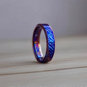 May include: A close-up of a ring with a vibrant blue and purple marbled design. The ring has a dark brown band and a flat top with a textured, swirling pattern. The ring is a unique piece of jewelry.