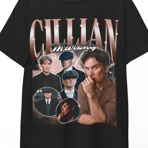 Peut inclure: T-shirt noir avec un graphisme de style vintage de Cillian Murphy. Le design comprend plusieurs images de l'acteur et le nom "Cillian Murphy" dans une police stylisée. Le t-shirt est suspendu à un cintre en bois.