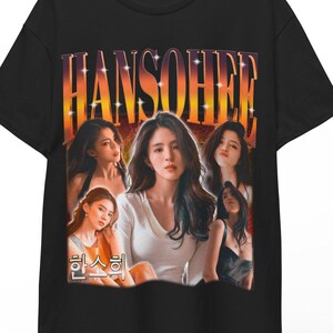 Könnte beinhalten: Schwarzes T-Shirt mit einer Grafik einer Frau und dem Namen "HANSOHEE" in orangefarbenen Buchstaben. Das Design enthält mehrere Bilder der Frau. Das T-Shirt hängt an einem Holzkleiderbügel.