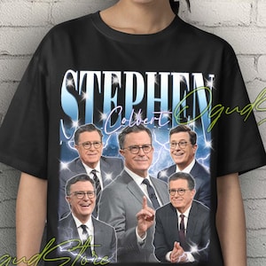 May include: Black unisex t-shirt featuring a graphic of Stephen Colbert in various poses. The design includes the name "Stephen Colbert" in a stylized font with a blue lightning effect. The shirt has short sleeves and a crew neck.