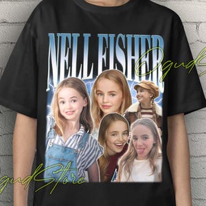 Puede incluir: Camiseta unisex negra con un retrato de Nell Fisher y el texto "NELL FISHER" en azul, con un estilo retro. La camiseta tiene cuello redondo y mangas cortas. Las palabras "Unisex T-Shirt" están en amarillo en la parte superior.