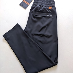Op de afbeelding: Zwarte sportbroek met elastische tailleband en een klein zakje. De merknaam "ZEGNA" is zichtbaar op de zak en een label. De broek is gemaakt van een gladde, donkere stof.