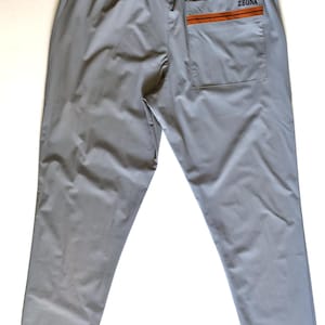 Op de afbeelding: Lichtgrijze broek met een elastische tailleband en een enkele achterzak. De zak is voorzien van een horizontale oranje streep en de tekst ZEGNA in het zwart gedrukt. De broek is gemaakt van een gladde, effen gekleurde stof.