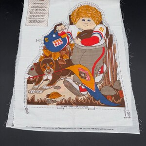 May include: A white fabric panel featuring a Cabbage Patch Kids design. The illustration depicts a child in a football uniform with a football and a dog. The design includes a helmet, a pennant, and the text "Leave Open for Stuffing."