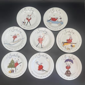 May include: A set of eight white ceramic plates featuring various illustrations of Santa Claus in red attire. Each plate displays the text Santa Baby and unique holiday-themed scenes, including a car, a surfboard, a Christmas tree, and a parachute.