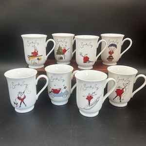 May include: A set of eight white ceramic mugs, each featuring a unique illustration of a character in a red outfit and the script text Santa Baby. The mugs have a flared rim, a curved handle, and a pedestal base, arranged in two rows.