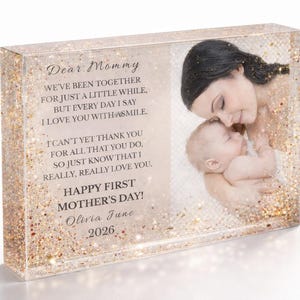 Peut inclure: Bloc de résine transparent rectangulaire avec des paillettes dorées et une photo d'une mère et de son bébé. Le texte dit "Chère maman, Bonne fête des mères !" avec le nom Olivia June et l'année 2026.