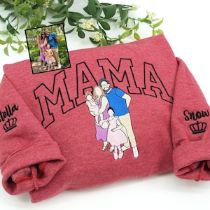 May include: A red sweatshirt with the word "MAMA" embroidered in black. The sweatshirt features a family portrait embroidery and the names "Stella" and "Snow" with crowns on the sleeves. The sweatshirt is folded.