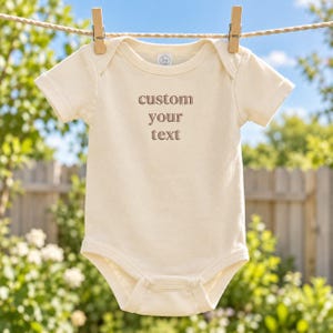 ベビーボディスーツへのカスタム刺繍テキスト - 赤ちゃんの苗字入り - 乳幼児用パーソナライズコットンボディスーツ - 誕生日や記念日のギフト