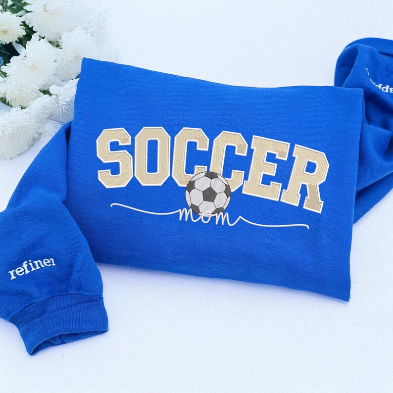 Royal blue Soccer Mom sweatshirt featuring bold varsity cream lettering and soccer ball in the center, with personalized sleeve embroidery “refiner.” Stylish and sporty hoodie for soccer moms cheering on kids at matches, cozy embroidered sweatshirt for game days.