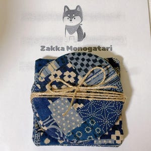 May include: A stack of blue and white patterned coasters tied with twine. The coasters have various geometric and floral designs. The text "Zakka Monogatari" is above the coasters, with a cartoon dog illustration.