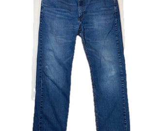 May include: A pair of medium-wash blue denim jeans featuring a classic five-pocket design, a button fly closure, and copper-toned rivets. The fabric displays subtle fading along the thighs and knees, with a straight-leg cut and stitched seams.