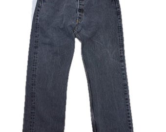 May include: A pair of charcoal grey denim jeans featuring a button-fly closure, five-pocket styling, and a straight-leg cut. The fabric has a faded wash with visible stitching along the seams, belt loops, and a metal button at the waist.