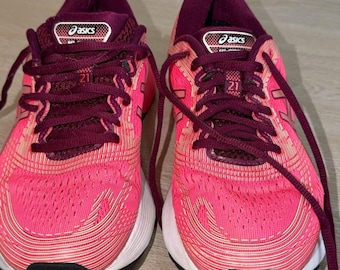 May include: A pair of Asics Gel-Nimbus 21 running shoes in bright pink with dark maroon laces, tongues, and inner lining. The shoes feature a white midsole, a black outsole, and the Asics logo on the tongue with the number 21 printed below.