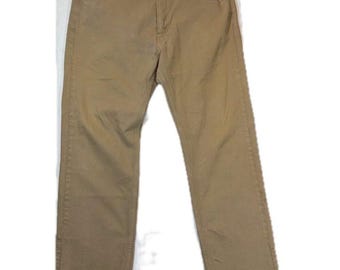 May include: A pair of tan-colored denim jeans featuring a classic five-pocket design, a button fly closure, and copper-toned rivets at the pocket corners. The pants have a straight-leg cut with visible tonal stitching throughout the fabric.