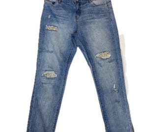 May include: Medium-wash blue denim jeans featuring a mid-rise waist, a button and zipper fly closure, and distressed areas on the thighs and knees. The distressed sections are embellished with gold-toned sequins for a textured finish.
