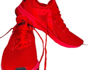 May include: A pair of bright red Puma athletic sneakers featuring a mesh upper, matching red laces, and a black Puma logo on the tongue. The shoes have a streamlined silhouette with a textured red sole and a small black accent on the heel.