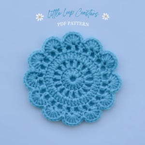 Pode incluir: Uma base de copo de crochê azul claro, com um design circular e borda ondulada. O texto "Little Loop Coasters PDF Pattern" é exibido acima. A base de copo tem aproximadamente 10 cm de diâmetro.