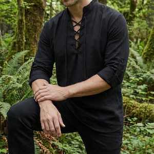 Pode incluir: Camisa preta de manga comprida com gola mandarim e frente com atacadores. As mangas est&atilde;o enroladas at&eacute; aos cotovelos. A camisa &eacute; feita de um tecido macio e respir&aacute;vel. A camisa faz parte de uma cole&ccedil;&atilde;o de roupas.
