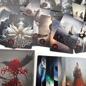 Puede incluir: Un juego de cartas de tarot con ilustraciones en blanco y negro y texto rojo. Las cartas presentan una variedad de im&aacute;genes, incluyendo una mujer con un vestido blanco, un &aacute;rbol, un barco y un cuervo. Las cartas est&aacute;n dispuestas en un c&iacute;rculo alrededor de una caja negra con texto rojo que dice "The Mighty Runes".